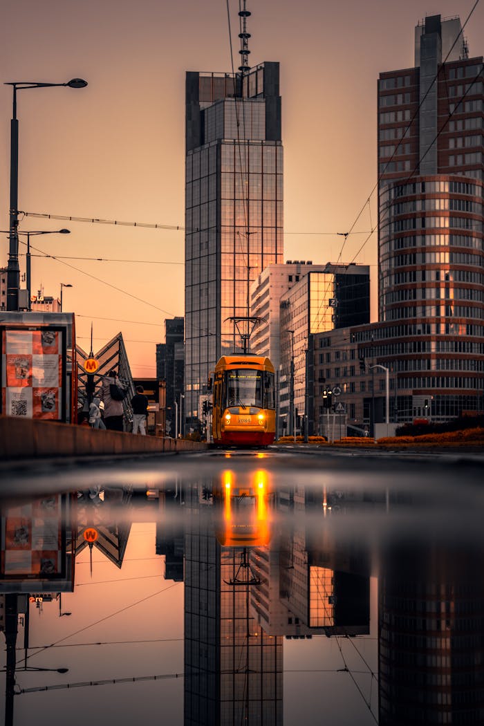 A vibrant city street in Warsaw with a tram and skyscrapers reflecting during sunset.